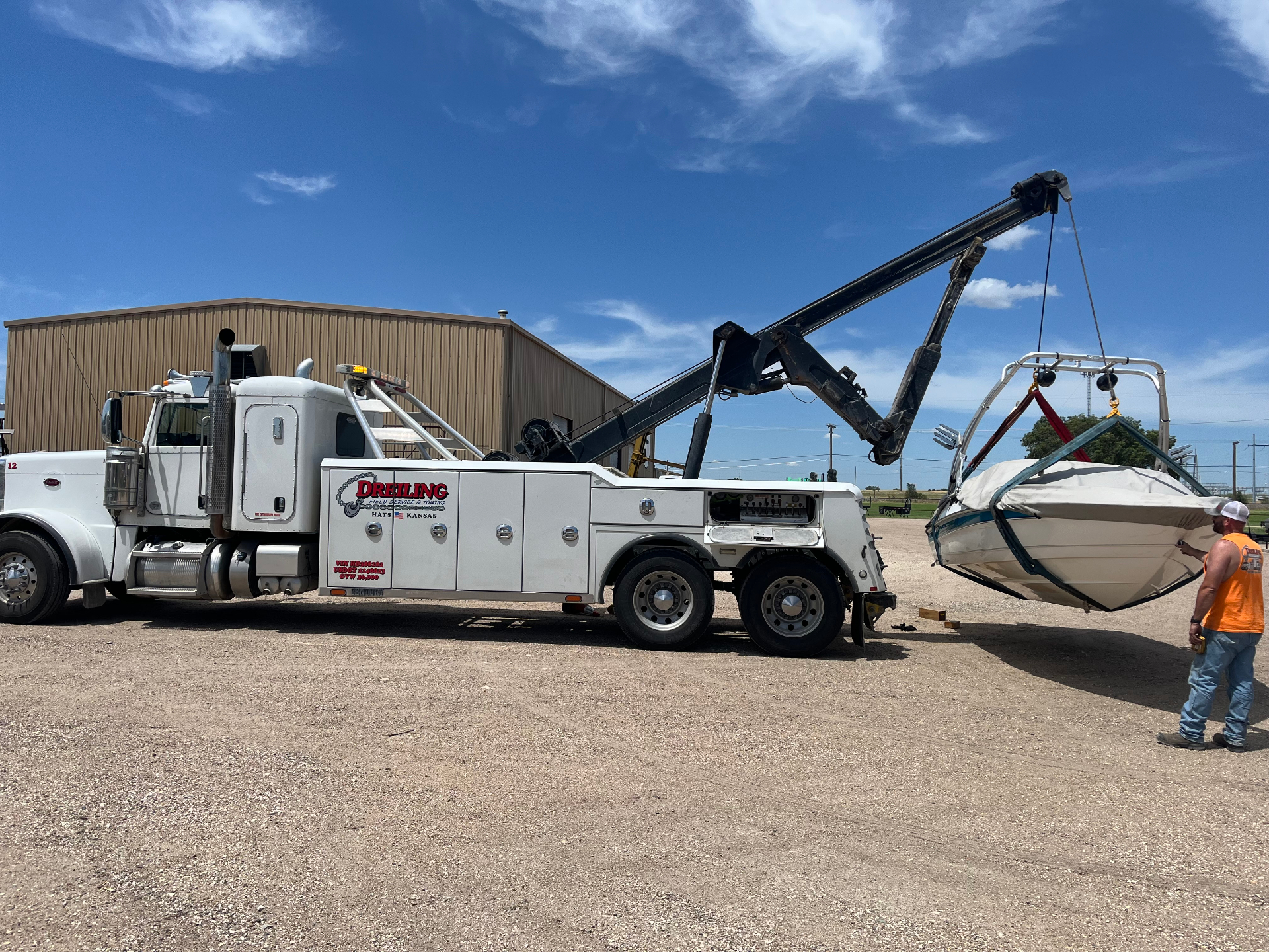 Dreiling white Peterbilt heavy wrecker using its boom to sling-lift a damaged boat at the shop in Hays, Kansas
